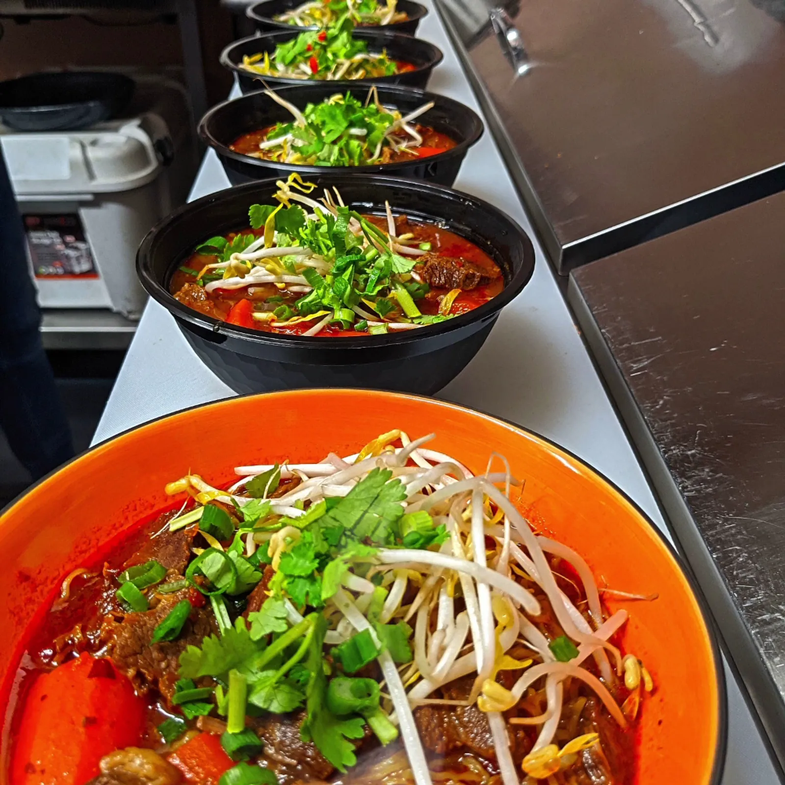 Row of Cambodian beef stew bowls on a stainless steel kitchen counter at Kitchen 8 Hastings