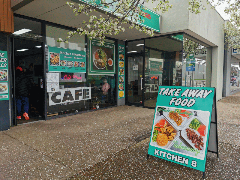 Kitchen 8 Hastings exterior storefront with green signage and A-frame takeaway sign on wet footpath