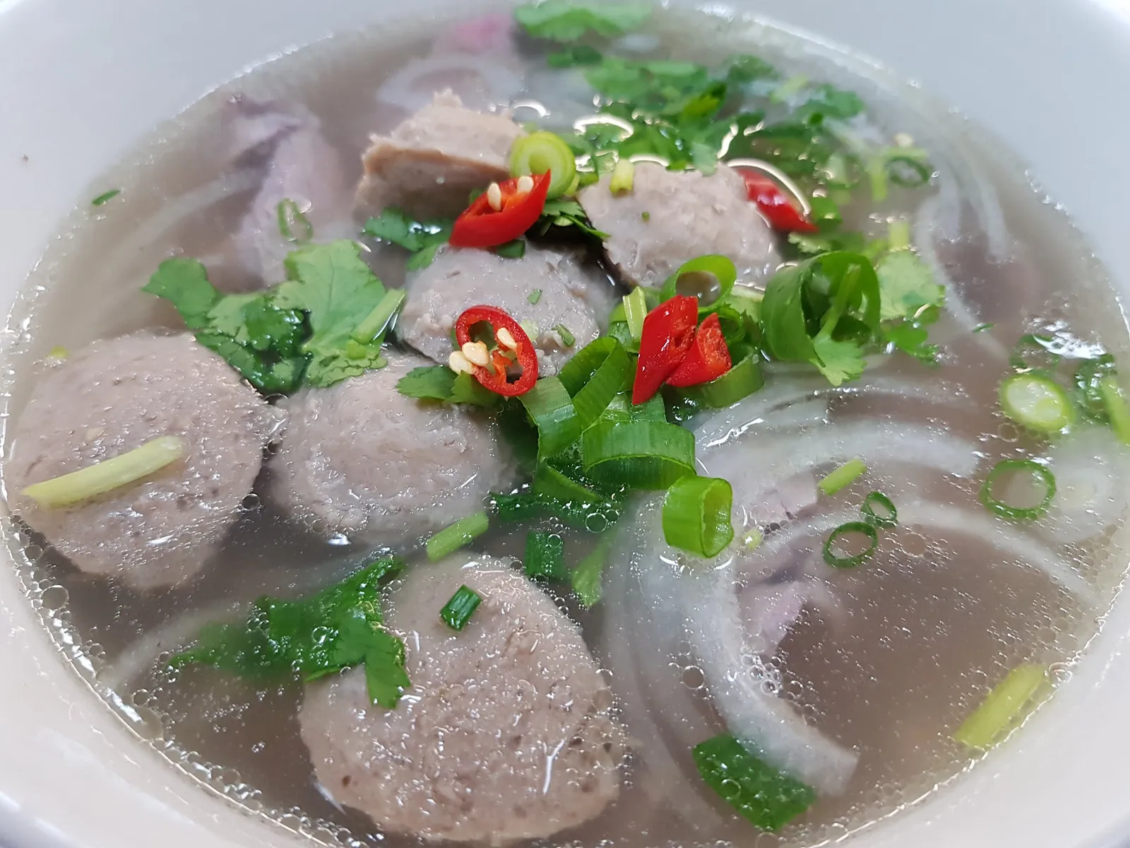 Vietnamese pho with beef balls, noodles, chili and fresh herbs in a white bowl